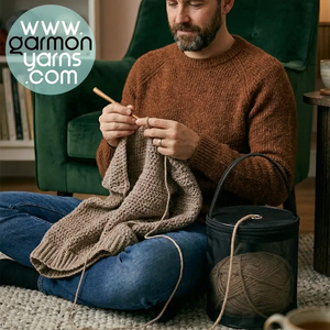 Bolsa dispensadora de lana - Garmon - hombre sentado en el suelo sobre una alfombra tejiendo un jersey a ganchillo con bolsa de lana negra